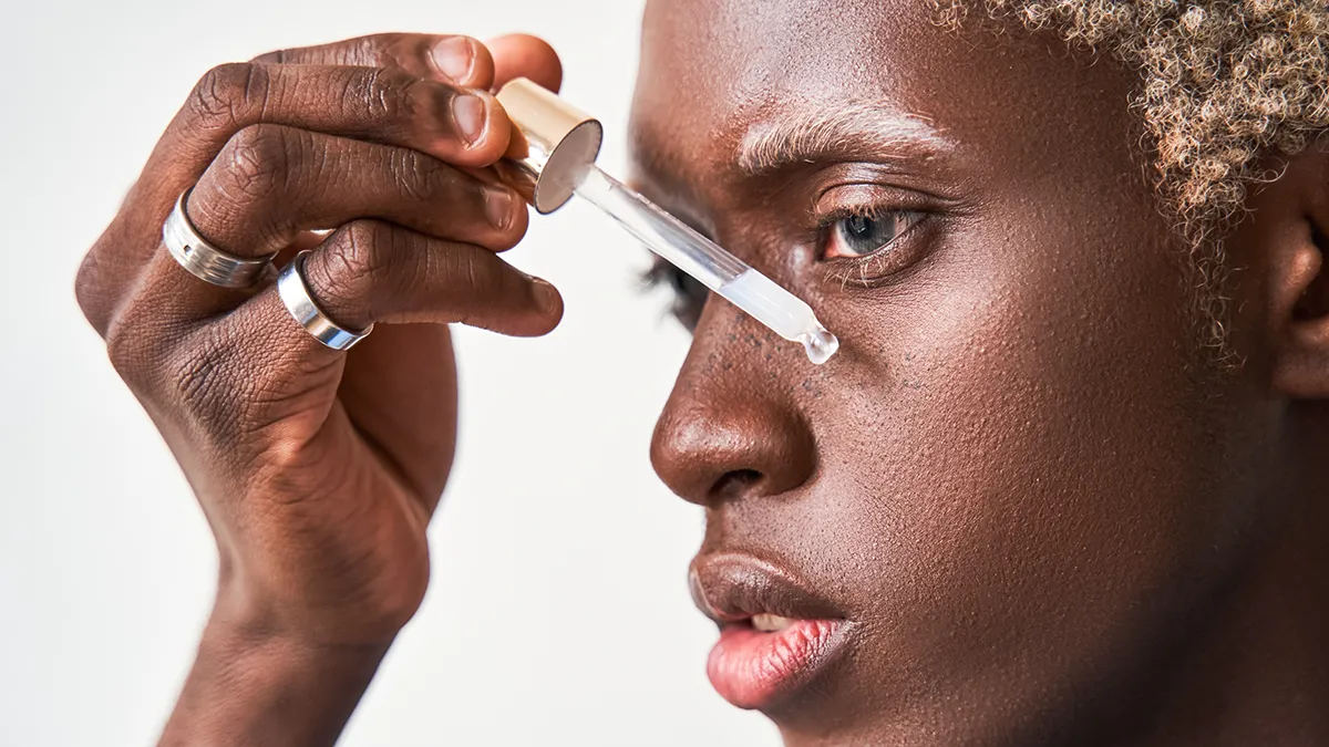 An African-American man with blond hair and eyebrows applying FAQ red light peptide serum